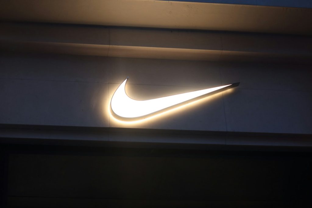 Illuminated white Nike logo Swoosh on a dark store facade at dusk