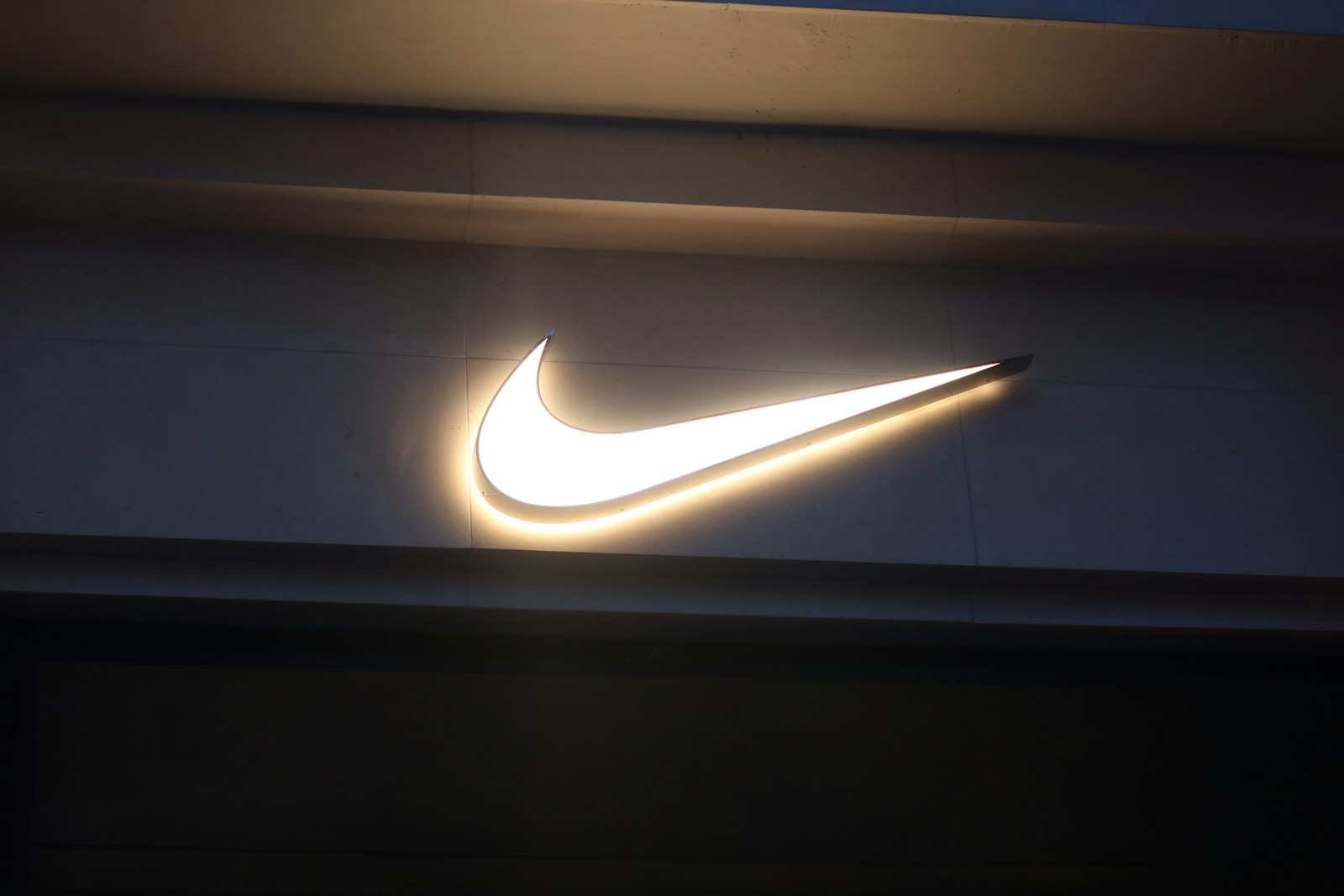Illuminated white Nike logo Swoosh on a dark store facade at dusk